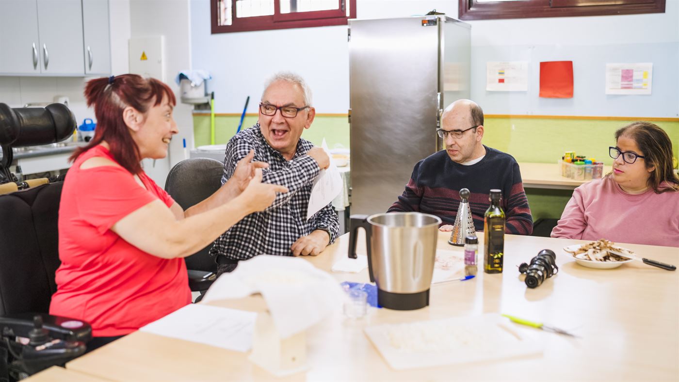 Four adults laughing and talking around a table as they prepare food together