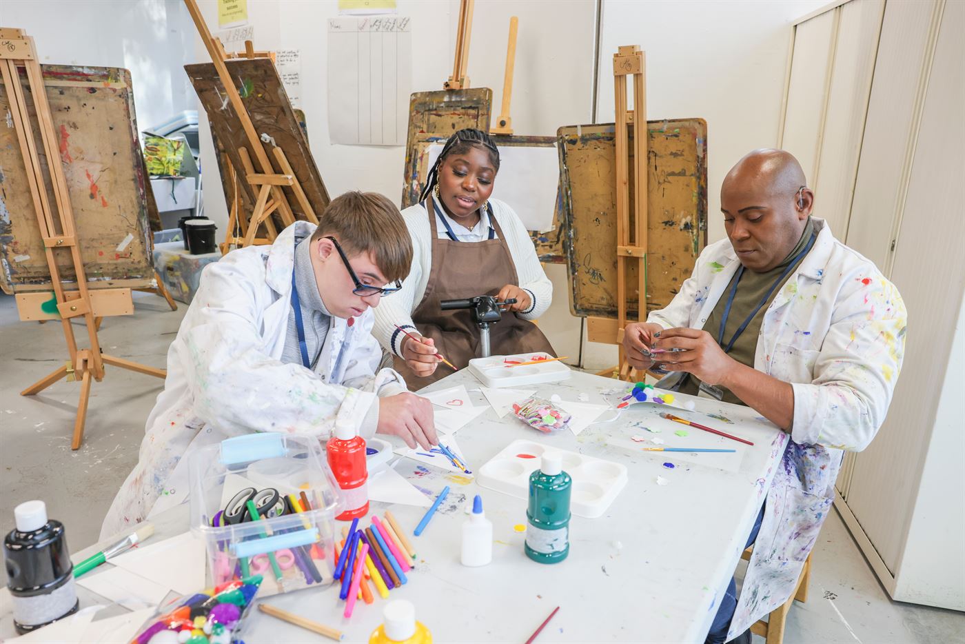 Three adults painting and doing crafts together at a table in an art studio